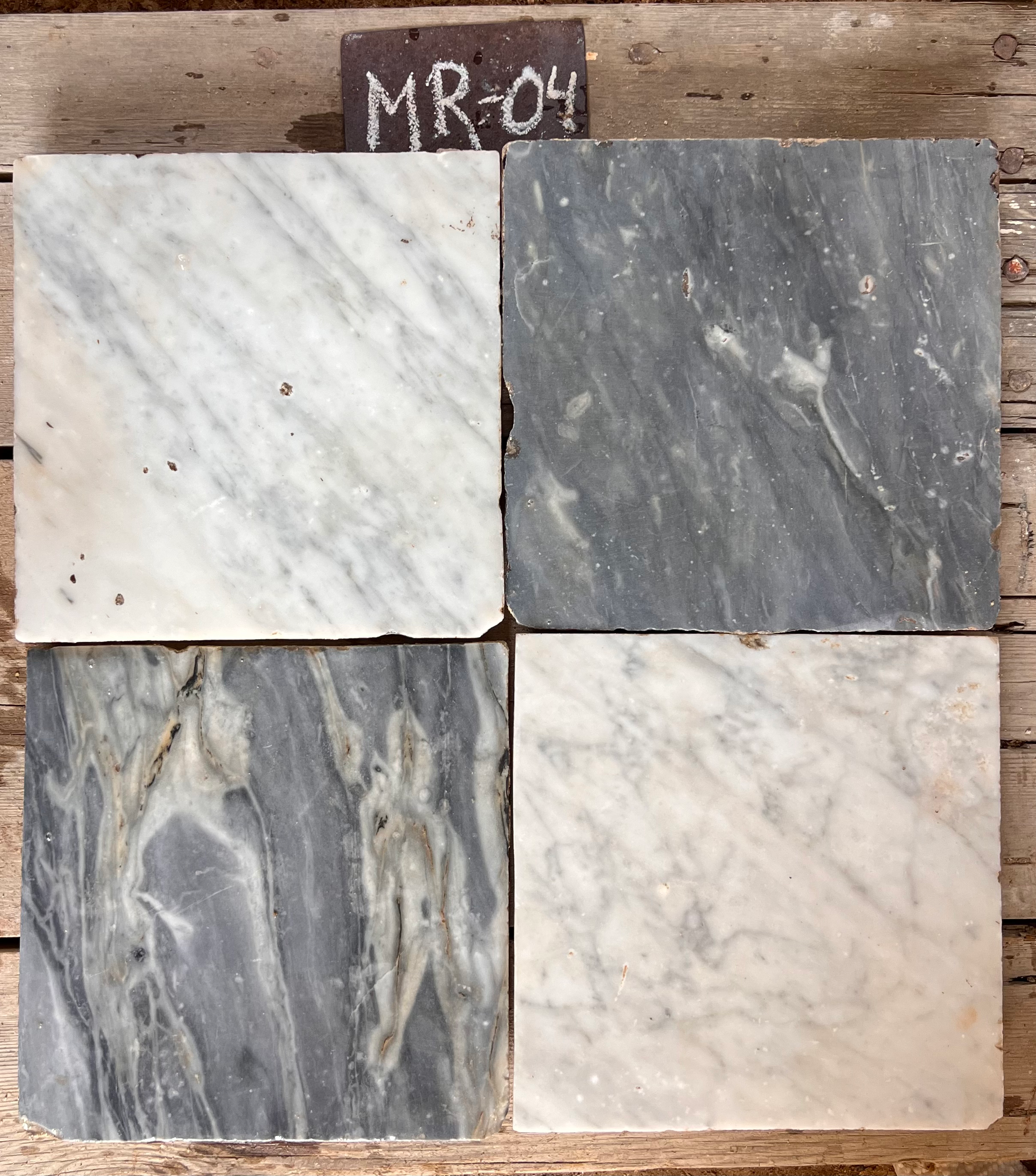 Cuatro piezas de mármol recuperado mostrando variación entre gris oscuro, blanco con venas y beige dorado, formato 26x26 cm