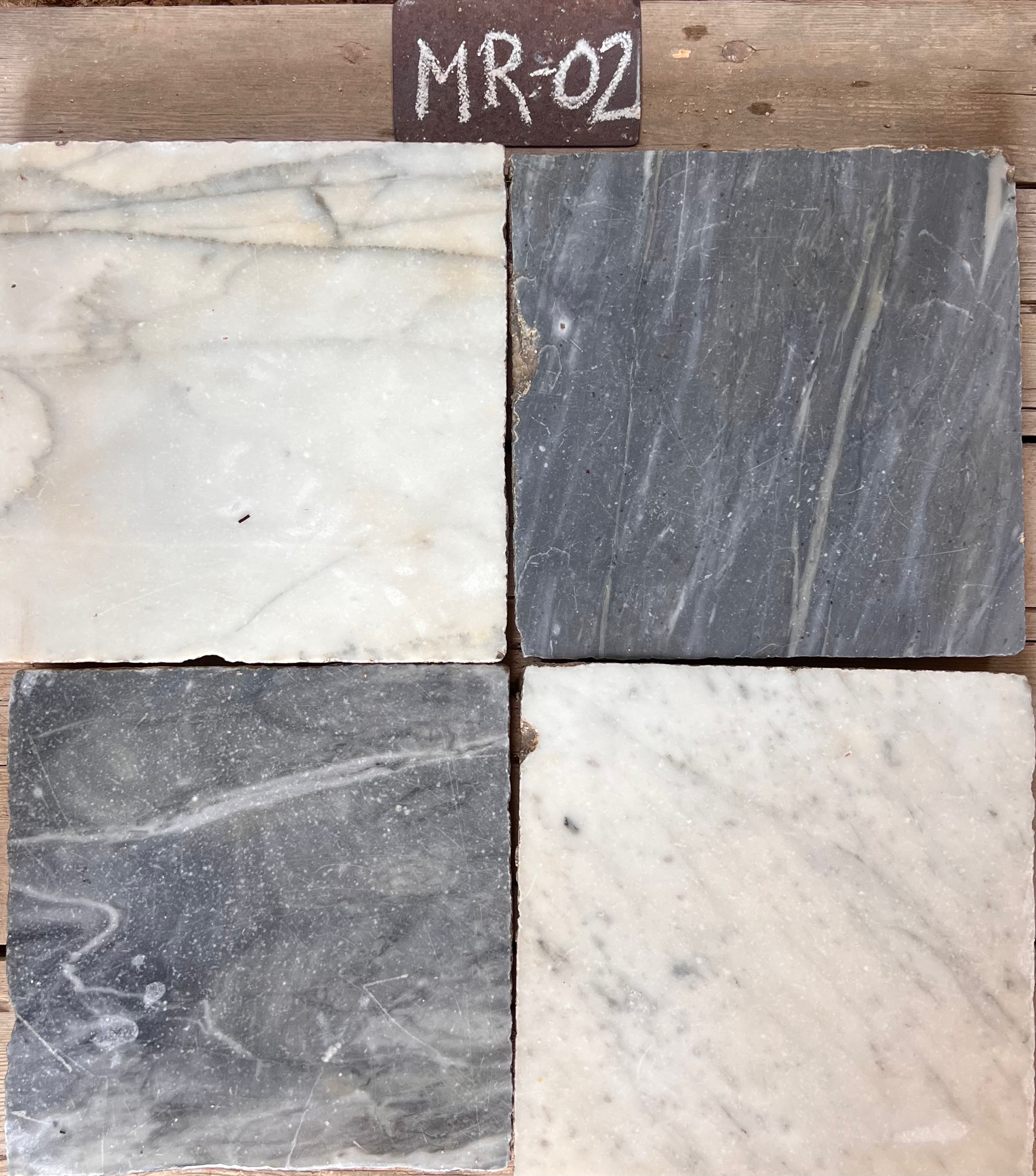 Cuatro piezas de mármol recuperado mostrando variación entre blanco crema, gris medio y gris oscuro, formato 27x27 cm