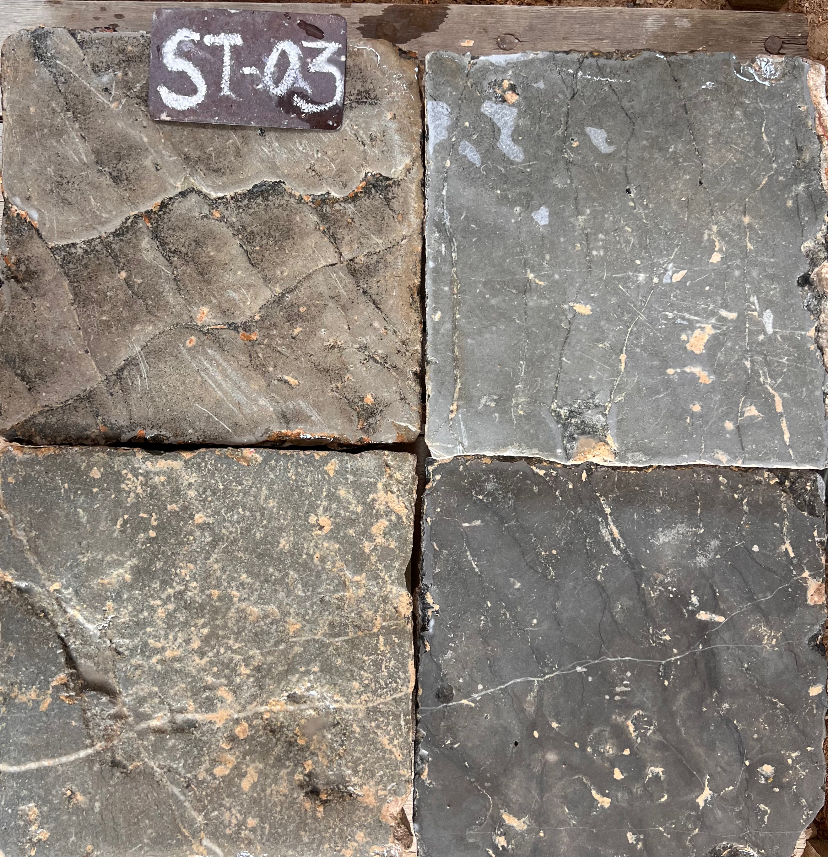 Cuatro piezas de piedra natural recuperada en gris oscuro con superficie rugosa, formato 28x28 cm