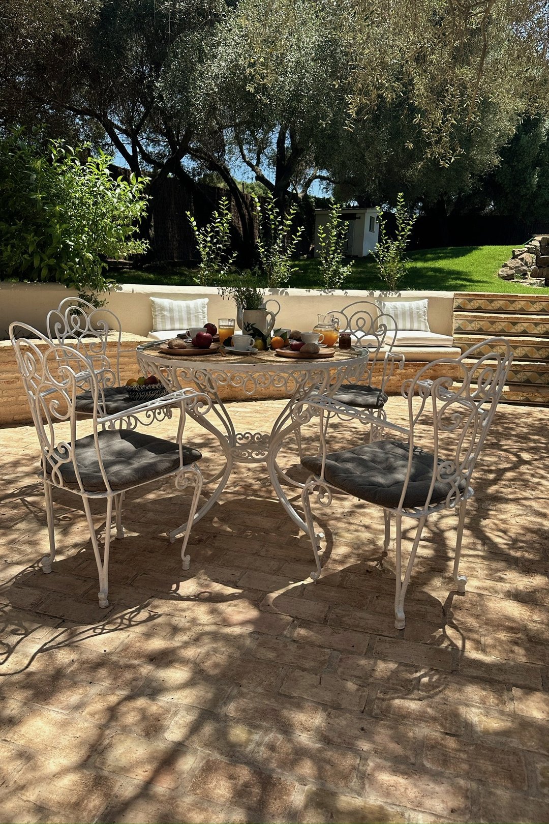 Mesa y sillas de forja recuperadas, servidas para el desayuno en un patio de barro entre olivos